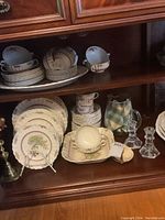 China cups, saucers, plates, meat platter, bowls displayed in wooden cabinet shelf.