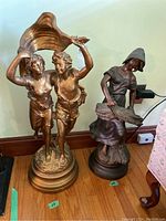 Photo showing both statues side by side on the floor: bronze female statue on the right, plaster statue of boy and girl on the left under a large shell.