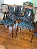 Set of four teak framed dining chairs with upholstered seats and backs, showing abstract patterned fabric in green, peach, and beige tones on hardwood floor.