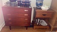 Frontal view of four-drawer dresser and side table with decorative pottery on top.
