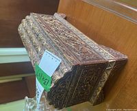 Side angle showing detailed ornate carvings and curved lid of the wooden treasure chest with colored dot inlays, some missing.