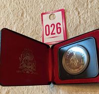 Open red velvet lined case with gold embossed Calgary coat of arms and dates 1875-1975, showing the commemorative silver dollar inside a protective holder.