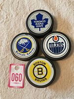 Four NHL vintage hockey pucks from 1985-1992 with Toronto Maple Leafs, Buffalo Sabres, Edmonton Oilers, and Boston Bruins logos visible.