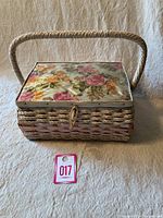 Front view of closed wicker sewing basket with floral laminated lid and handle.