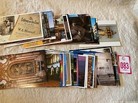 Two stacks of various European postcards spread out on a fabric surface, showing multiple colorful scenes mostly architectural and cultural.