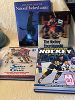 Four large hardcover hockey books displayed on a beige surface clustered together.
