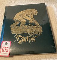 Front cover of the book showing gold embossed great ape illustration on a dark background, sealed in plastic.
