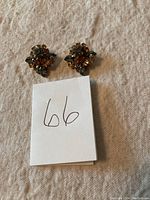 Full view of both earrings placed on fabric with a white note labeled '66'