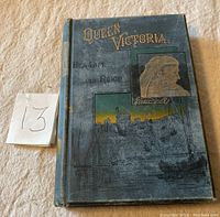 Front cover of the 1888 hardcover book showing the title, author's name, and pictorial illustration of Queen Victoria and harbor scene.