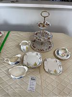 Full lot photo showing Aynsley three-tiered cake plate, eight cake plates, creamer, cream and sugar set, and teacup with saucers