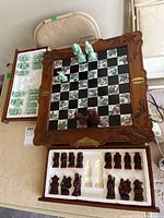 Top-down view of the entire chessboard showing carved wooden frame, composite tile board with black and printed squares, and chess pieces partially placed and stored in drawers.