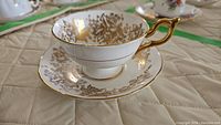 Side view of white teacup with gold floral gilding and gold handle resting on matching saucer