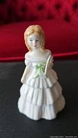 Front view of the Royal Doulton Julie figurine showing detailed facial features, white tiered dress with green sash, and fan held in hand.