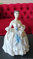 Front view of the Royal Doulton Kelly figurine showing full figure in cream dress with blue floral details and gold tag.