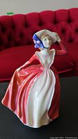 Front and side view of Royal Doulton 'Mary' figurine showing detailed face, bonnet with blue ribbons, and flowing red and white dress.