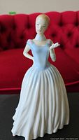 Front side view of Royal Doulton figurine against red background showcasing dress details and pose