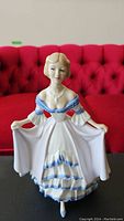Front view of Royal Doulton porcelain figurine showing full figure in white and blue dress with hands holding skirt
