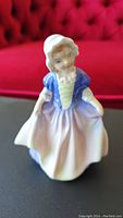 Front view of Royal Doulton Dinky Do figurine with bonnet, blue jacket, and purple/white dress.
