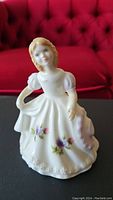 Front view of Royal Doulton March figurine showing detail of floral decorations on dress and facial features.