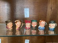 Six Royal Doulton Toby character jugs lined up on a glass shelf, showing full set