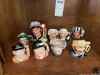 Front view of all 9 Royal Doulton Toby character mugs arranged on a wooden surface, showing detailed faces and accessories like hats, feathers, and pipes.