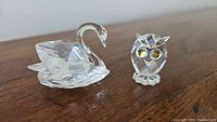 Both Swarovski crystal figurines shown together, swan on left and owl on right.