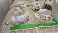 Four teacups and saucers arranged on a quilted surface, showing various floral patterns and gold trim.