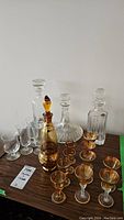 Three crystal decanters and one amber decanter with stopper, along with six amber gold rimmed aperitif glasses and four clear aperitif glasses on a wooden table.