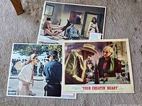 Three vintage lobby cards, two from 'The Lady in the Car' and one from 'Your Cheatin Heart', displayed on a carpeted floor, showing character scenes.