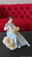 Full view of the vintage Royal Doulton figurine showing the seated woman weaving a basket, highlighting the elegant posture and detail of the dress and basket.