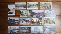 Photo showing all 15 antique postcards laid out on wooden floor, including various black-and-white and color-tinted images of cityscapes, historic buildings, and rural scenery.