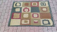 Area rug laid out on a paved surface showing different colored squares and rectangles in abstract design