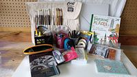 Overview of all art supplies, several packs mostly unused, paintbrushes, books, tape, drawing tools, and palette