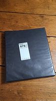 Black textured binder on wooden floor with label 876 on front