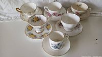 Overview of six fine bone china cups and saucers showing different floral patterns and gold trim, with one cup having visible crazing