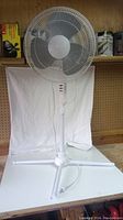 Full view of the white FOR LIVING oscillating pedestal floor fan with folding base set up on a table with a white sheet background.