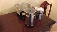 Photo showing Nespresso milk frother, coffee container, and fry basket on wooden table.