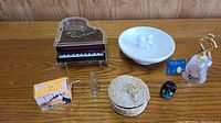 Full lot image showing piano music box, porcelain ring bowl, straw bowl, Coca-Cola bottle, lacquered dog figure, crystal bell, small glass bottle, and small boxed music box.
