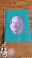 Green cover of dinner program with oval cutout displaying a portrait photo of Norman Jewison, featuring gold braided rope with tassels