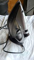 Sunbeam cordless iron placed on its charging base, showing power cord connection and side profile with control icons and water reservoir visible.