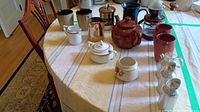 Top view of table showing all items arranged including coffee grinders, mugs, creamer pitchers, teapot, and tin.