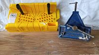 Photo showing both the blue Mastercraft bench vise and the yellow hand saw jig side by side on a wooden surface.