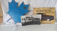 Photo showing all three items together: blue metal Maple Leaf, Empress Victoria steamship photo, and Merrickville Car Show sign