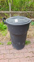 Front view of black Rubbermaid wheeled garbage can with lid on, slight wear visible on the surface.