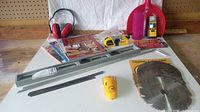 Complete set of woodworking supplies showing ear protection, stud finder, level, saw blades, sanding block, tape measure, dustpan, brush, and booklets on a wood surface with white backdrop.
