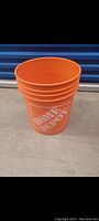 Four stacked orange Home Depot buckets with visible white logo on front.
