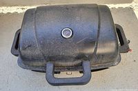 Closed view of the black portable electric BBQ grill with built-in thermometer on lid and handles on all sides.