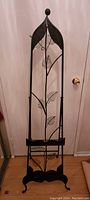 Front view of tall black metal easel with leaf pattern and curved legs.