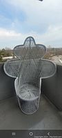 Front and angled views of large white wicker peacock chair placed on balcony, showing ornate tall backrest and rounded wide wings.