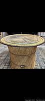 Front view of a round wicker table with clear glass top on a patterned rug.
